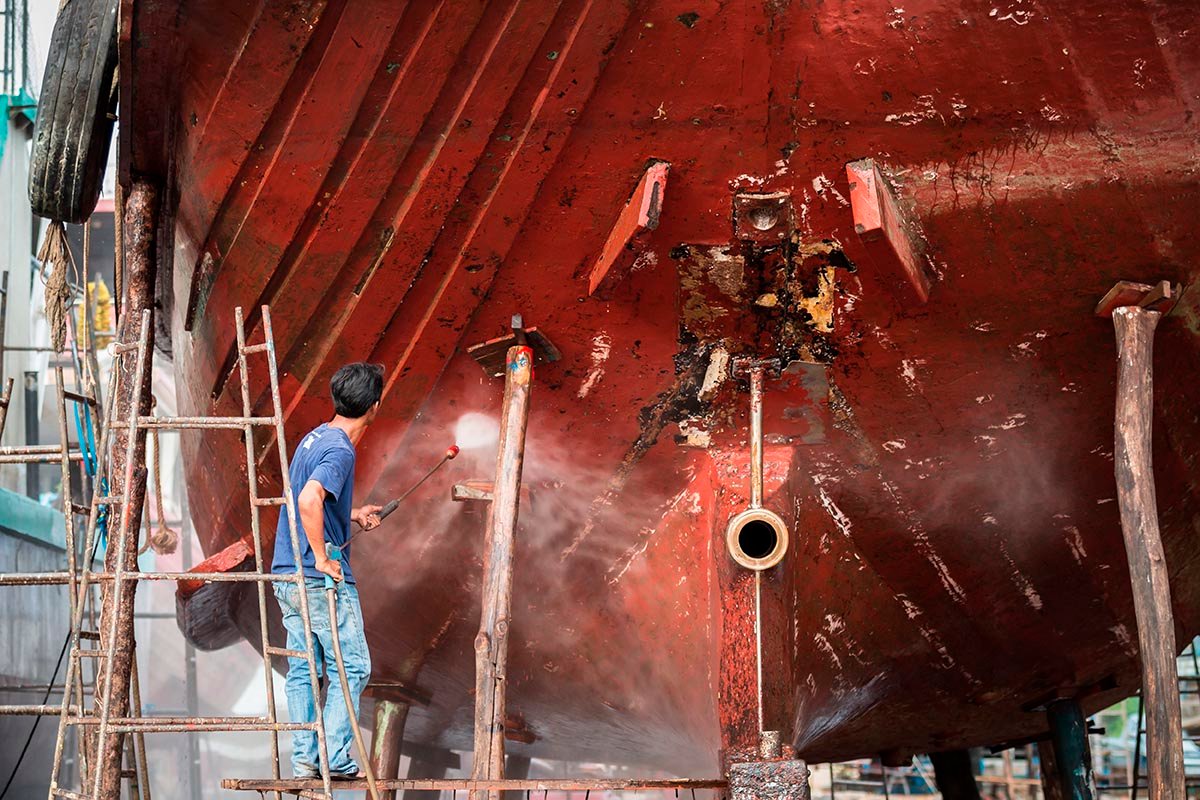 A man working on pressure washer to cleaning boat hull barnacles antifouling and seaweed at the harbor