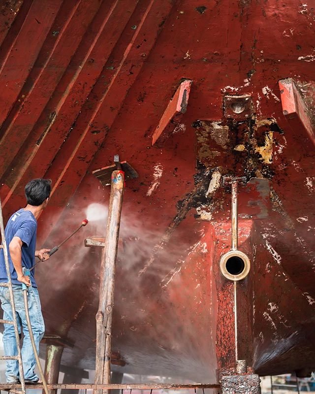 A man working on pressure washer to cleaning boat hull barnacles antifouling and seaweed at the harbor